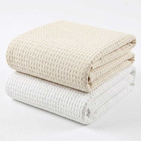 Pictured: Two waffle woven blankets neatly folded and stacked against a white background. The blanket on the bottom is in the shade "White" and the one on top is in the shade "Beige".