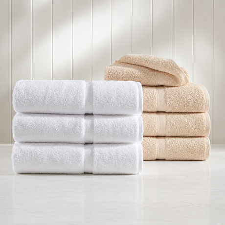 Pictured: Two Crown Touch Towel sets neatly folded and stacked on a white surface against cream shiplap. In the foreground is the white towel set and in the background is the beige towel set.