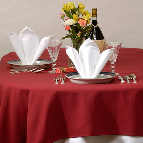 Pictured: Decorated banquet table with plates, glasses, silverware, a flower bouquet and a bottle of alcohol. On the plates are the white Dynasty Napkins which are folded very fancy in order to free stand. 