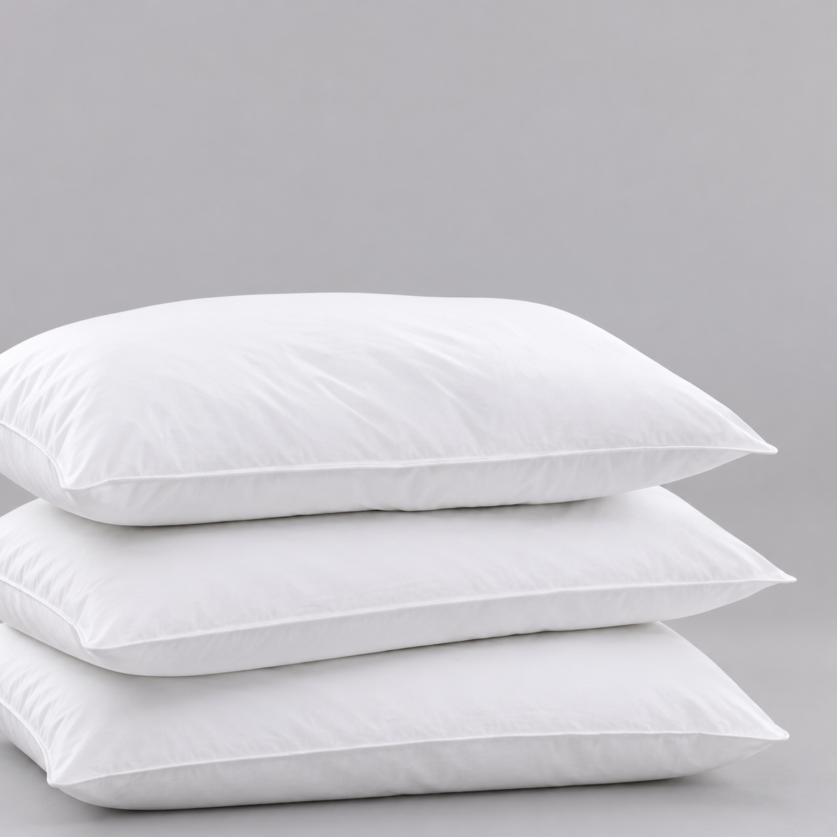 Pictured: 3 fluffy white pillows laid down and stacked on top of each other against a gray background. The product featured is the Gold Label Hospitality Pillow.