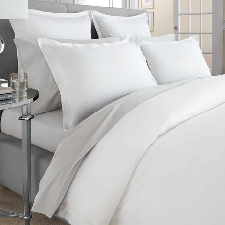 Pictured: Nicely made white bed on a gray bed frame with a mirrored side table to the left. The bedding features the Gryphon Supima Cotton T-360 sheets.