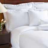 Pictured: Nicely made white bed on a wooden bedframe with a matching nightstand. The bedding features the Magnificence T-310 sheets.