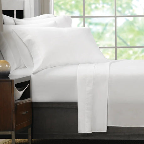 Pictured: The Martex Ultra Touch white sheets on a nicely made bed in front of a window and next to a nightstand.