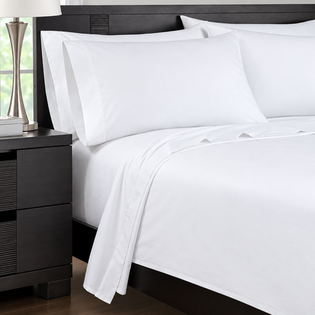 Pictured: Nicely made white bed on a dark wood frame with a matching nightstand to the left. The bed features the Martex Dry Fast t-200 Sheets.
