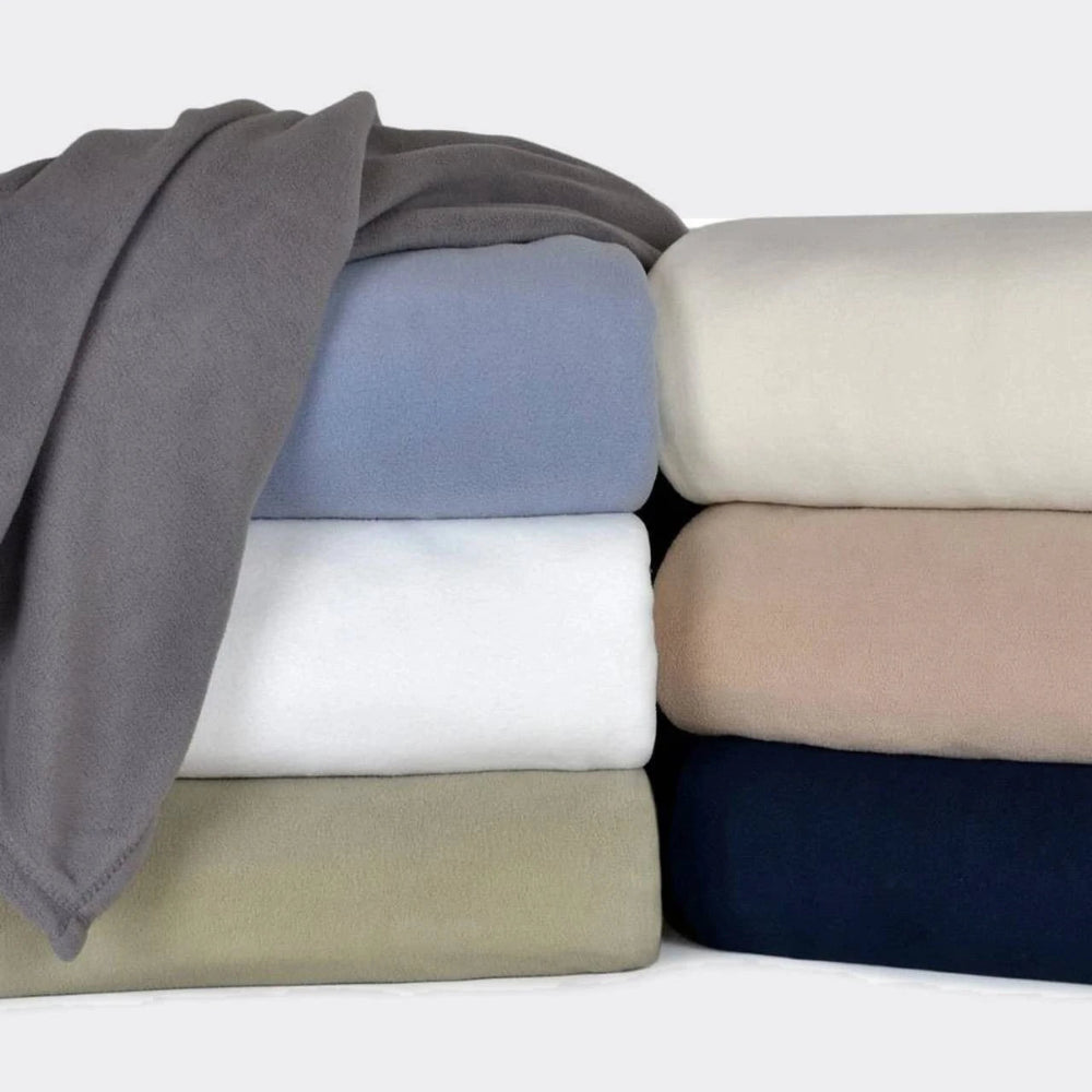 Pictured: Two stacks of neatly folded microfiber blankets in multiple colors, with one blanket folded over the left stack against a white background. The shades of the left stack from top to bottom; Smoke, Periwinkle, White and Sage. On the right top to bottom; Cream, Linen and Navy.