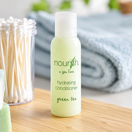 Pictured: Small standing green bottle with a clear cap in the forefront of a bathroom setting. The bottle is part of a spa line called Nourish, and it is the hydrating conditioner with green tea. The bottle holds 1 fluid oz. (30 mL)