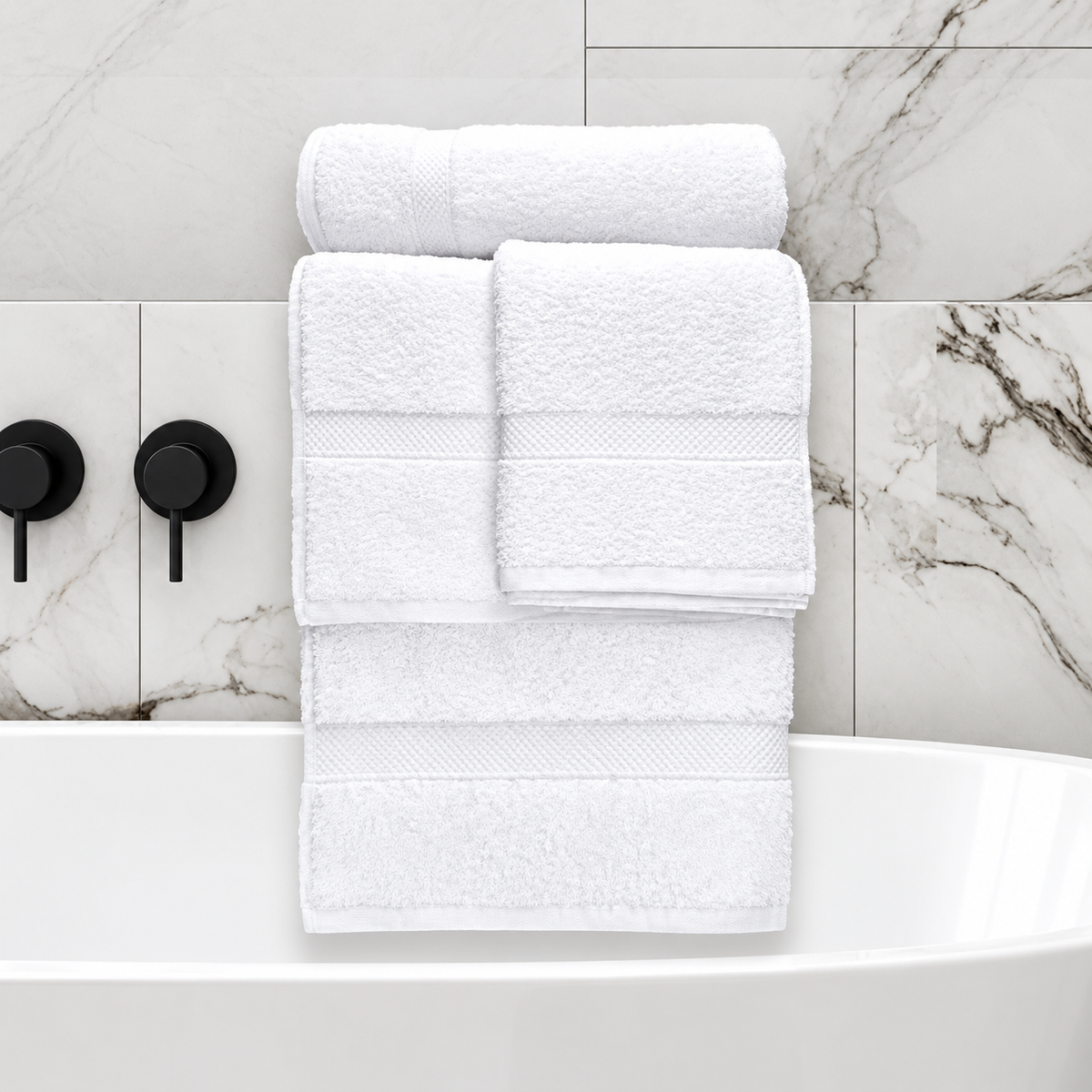 Pictured: Full Nuvola towel collection on a bathroom shelf above a free standing tub. These white towels have  decorative dobby bordering and the collection consists of a washcloth, hand towel, bath towel and bath mat.