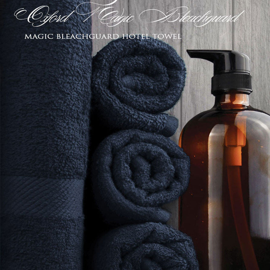 Rolls of navy blue towels next to a brown bottle on a wooden surface with 'Oxford Towel Company' branding.