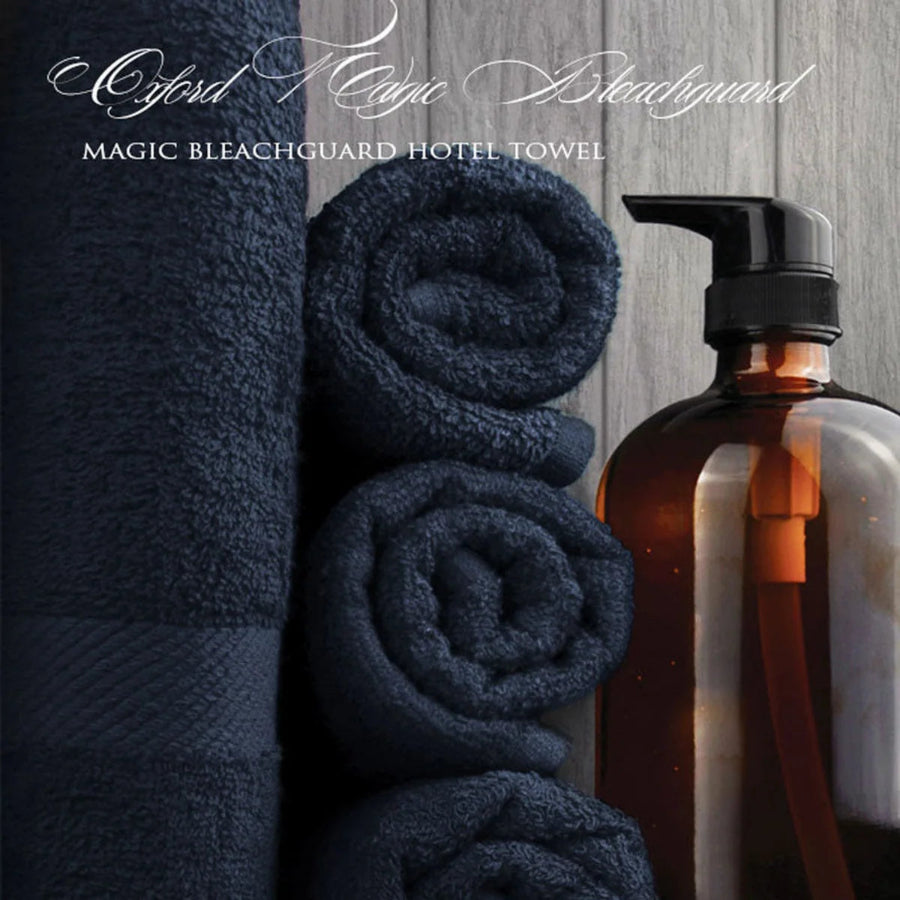 Pictured:  White cursive text that says "Oxford Magic Bleachguard" and then a serif font below that says "MAGIC BLEACHGUARD HOTEL TOWEL"
You can see 4 navy blue towels, 3 of which are neatly rolled and stacked while the other one is standing on the left. There is a brown dispenser bottle to the right.