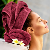 Pictured: Model leaning back on a neatly rolled towel, with their hair wrapped in the same colored towel. This is the Oxford Salon and Spa Towel in the shade Burgundy.