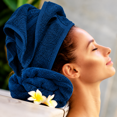 Pictured: Model leaning back on a neatly rolled towel, with their hair wrapped in the same colored towel. This is the Oxford Salon and Spa Towel in the shade Navy.
