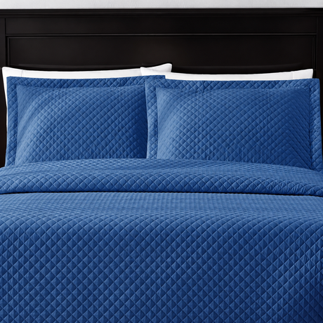 Pictured: Blue bedding on a dark wood bedframe. The bedding features the Radiance Diamond Quilted Sham, which has a diamond stitch creating a textured pattern.