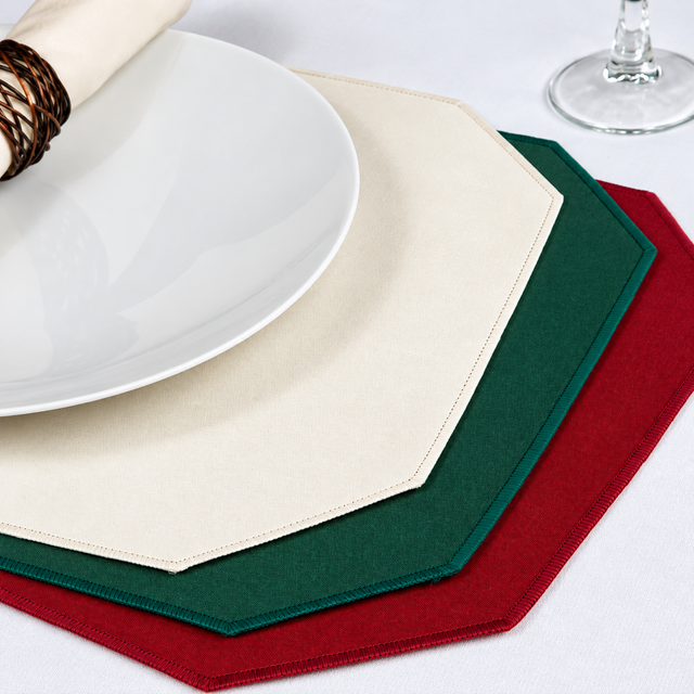 Pictured: Three of the premier placemats spread on a white table with a plate on top and a wine glass in the top left corner. 
