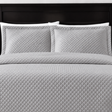Pictured: Grey bedding on a dark wood bedframe. The bedding features the Radiance Diamond Quilted Sham, which has a diamond stitch creating a textured pattern.
