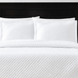 Pictured: White bedding on a dark wood bedframe. The bedding features the Radiance Diamond Quilted Sham, which has a diamond stitch creating a textured pattern.