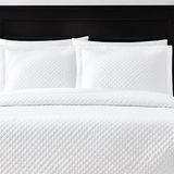 Pictured: White bedding on a dark wood bedframe. The bedding features the Radiance Diamond Quilted Sham, which has a diamond stitch creating a textured pattern.