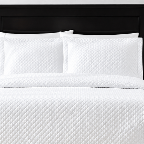 Pictured: White bedding on a dark wood bedframe. The bedding features the Radiance Diamond Quilted Sham, which has a diamond stitch creating a textured pattern.