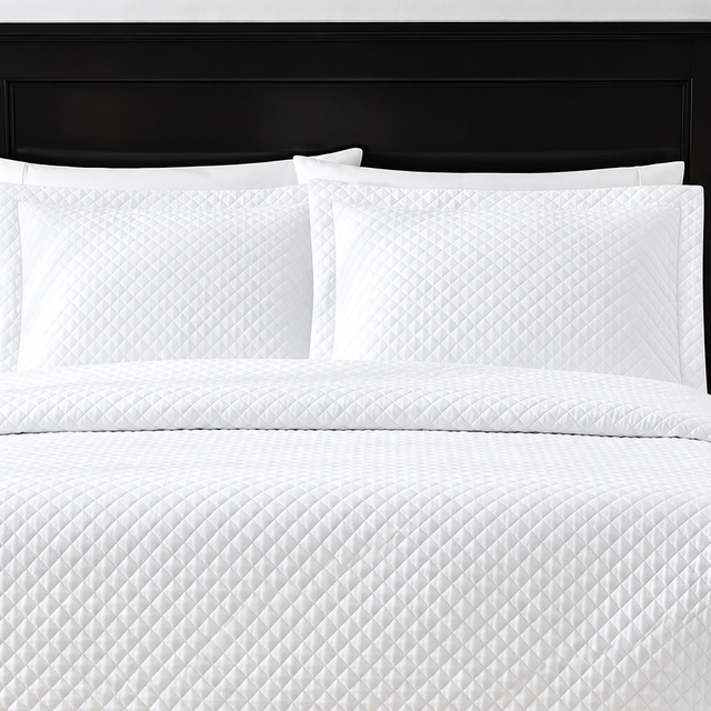 Pictured: White bedding on a dark wood bedframe. The bedding features the Radiance Diamond Quilted Sham, which has a diamond stitch creating a textured pattern.