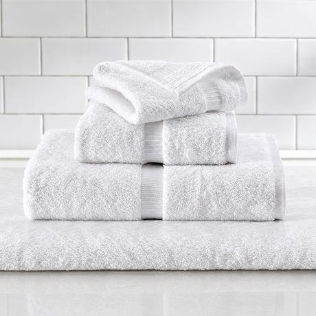 Pictured: Different white towels neatly folded and stacked on top of each other. They sit on a marble surface in front of white subway tile. The towels feature a vertical dobby border.