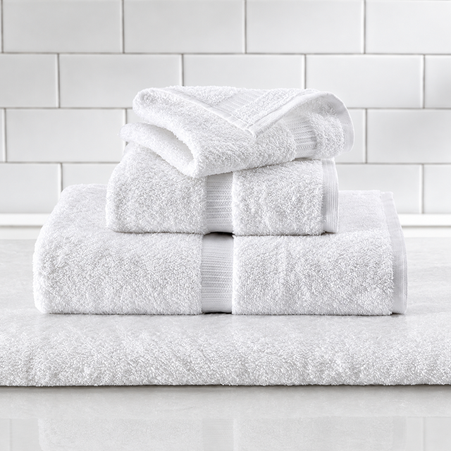 Pictured: Different white towels neatly folded and stacked on top of each other. They sit on a marble surface in front of white subway tile. The towels feature a vertical dobby border.