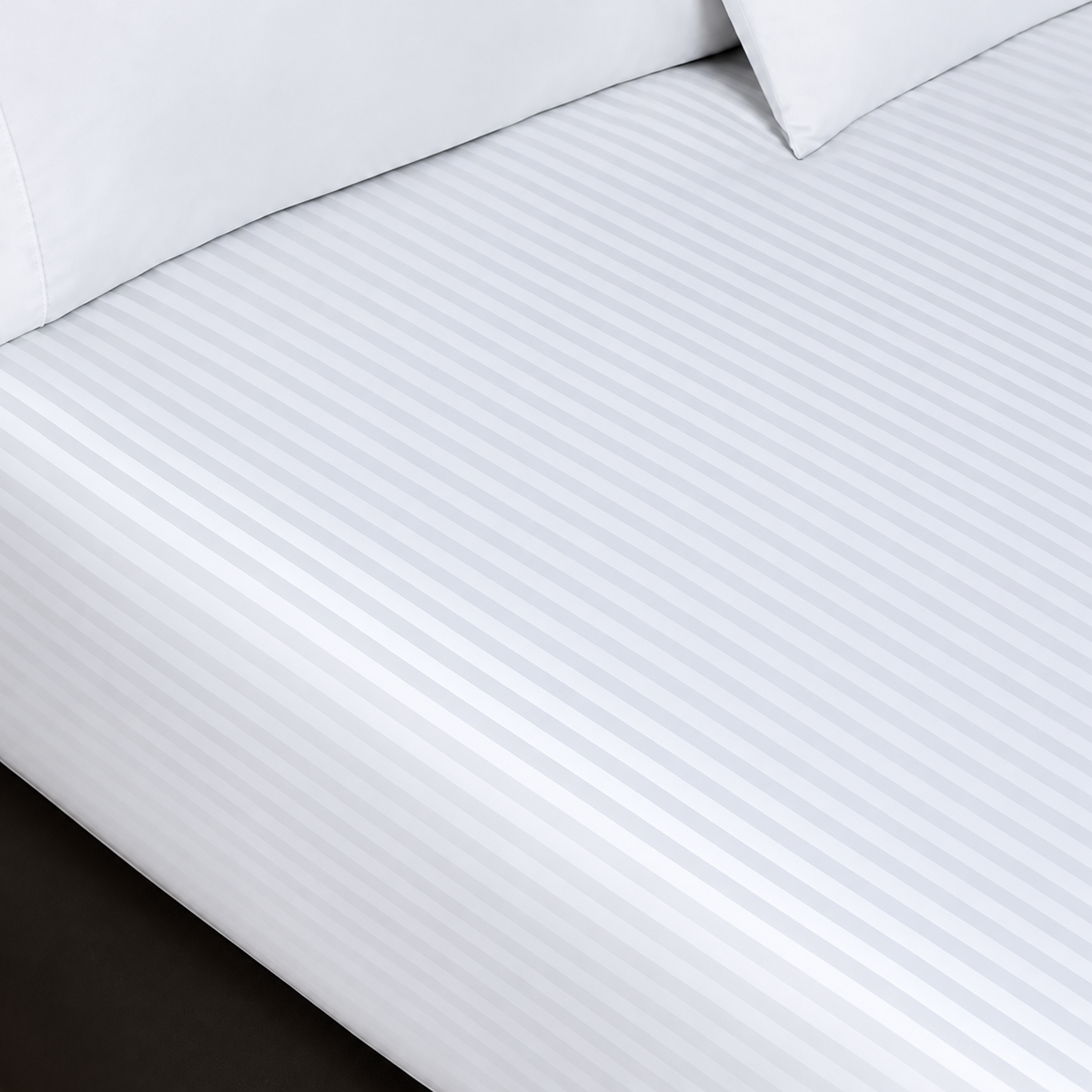 Pictured: White sheets with a striped pattern on a mattress. There are two pillows sitting on top of the sheets.