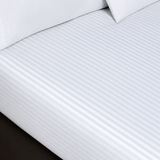 Pictured: White sheets with a striped pattern on a mattress. There are two pillows sitting on top of the sheets.