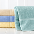 Pictured: On the left are 3 solid colored towels neatly folded and stacked. The colors from top to bottom are: Yellow (we do not carry this shade, Porcelain, Blue and beige. On the right is a folded towel standing up, leaning against the folded stack. This towel is in the shade Seafoam.