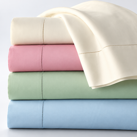 Pictured: A neatly folded stack of different colored bed sheets against a white background, with the top sheet draping  over the side. The colors from top to bottom are: Bone, Rose, Seafoam Green and Light Blue.