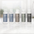 Pictured: Full Terra Pure Lemongrass mini collection lined up in a row on a marble surface. The products from left to right are: Conditioning Shampoo (blue label), Shampoo (blue label), Conditioner (bronze label), Body Wash (green label) and Lotion (dark grey label).