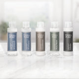 Pictured: Full Terra Pure Lemongrass mini collection lined up in a row on a marble surface. The products from left to right are: Conditioning Shampoo (blue label), Shampoo (blue label), Conditioner (bronze label), Body Wash (green label) and Lotion (dark grey label).