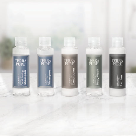 Pictured: Full Terra Pure Lemongrass mini collection lined up in a row on a marble surface. The products from left to right are: Conditioning Shampoo (blue label), Shampoo (blue label), Conditioner (bronze label), Body Wash (green label) and Lotion (dark grey label).