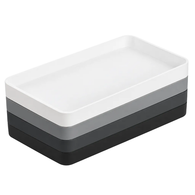 Pictured: Eco Contour Rectangular Amenity Trays stacked on top of each other against a white background. From top to bottom: White tray, Gray tray, Graphite tray and Black tray.