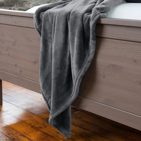 Pictured: A grey fluffy blanket draped over the wooden footboard of a bed.