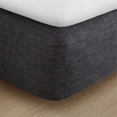Pictured: Dark grey fabric box spring cover against a wooden floor.