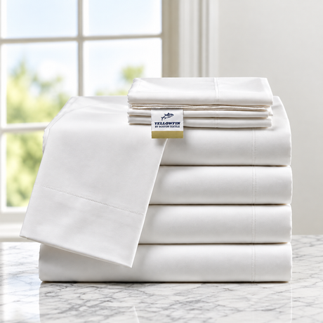 Pictured: Neatly folded white sheets stacked by size on a granite counter in front of a window. The label reads "YELLOWFIN by Boston Textile".